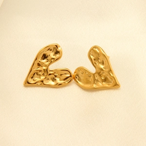 Detalle de aretes de corazón en oro de 18k con textura martillada sobre seda crema