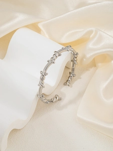 Detailopname van een zilveren C-vormige doornarmband op een elegante zijden achtergrond