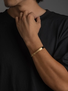 Detalle de brazalete dorado para hombre con grabado del Padre Nuestro y cruz religiosa