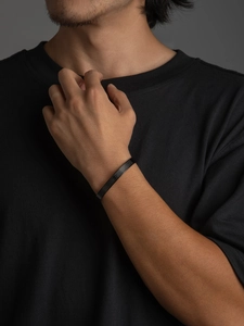 Detalle del brazalete de acero inoxidable negro mate con escrituras grabadas en muñeca de hombre