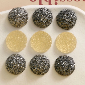 Detailed macro view of round druzy textured DIY resin charms in black and gold tones