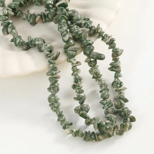 Close-up of green natural stone irregular beads on white decorative shell tray