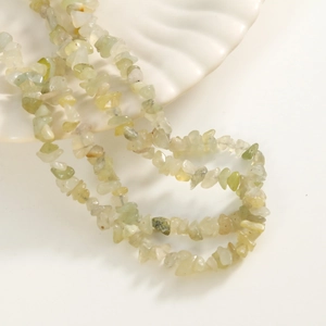 Macro shot of irregular natural green stone beads displayed on a white shell-shaped tray