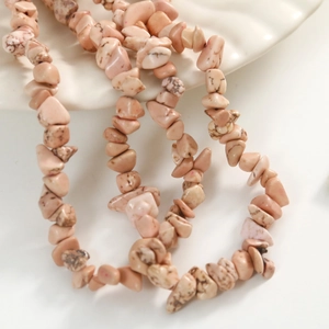 Macro detail of natural pink stone beads with brown veins on a white ceramic plate