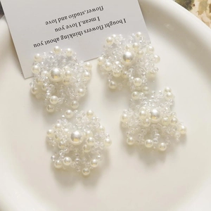 Dettaglio macro di orecchini a fiore fatti a mano con perle e cristalli su piatto bianco