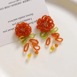 Détail de boucles d'oreilles fleurs tissées à la main en perles oranges et cristaux jaunes