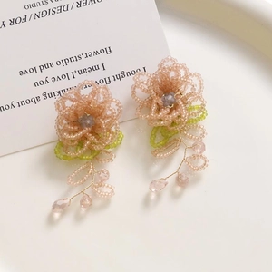 Détail macro de boucles d'oreilles fleurs en perles roses avec feuilles vertes et glands