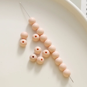 Detail of 8mm peach round acrylic beads scattered on a white ceramic plate for DIY crafts