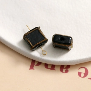 Macro shot of black square glass beads with gold painted edges and metal loop for DIY jewelry