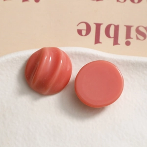 Macro shot of coral pink resin jewelry charms with spiral texture on a ceramic tray