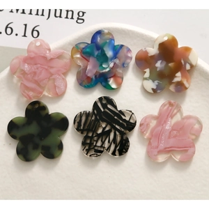 Close-up of colorful floral acetate charms for DIY jewelry making in a white ceramic dish