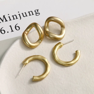 Minimalist matte gold C-shaped earrings with brushed metal texture on a white tray