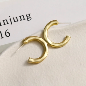 Detailed close-up of matte gold C-shaped earrings with unique hammered metal texture