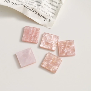 Détail de cinq breloques carrées en acrylique rose pailleté pour bijoux DIY et pinces