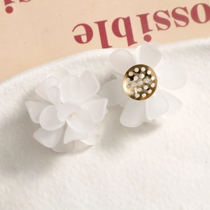 Macro shot of matte white acrylic flower earrings with golden metal back detailing