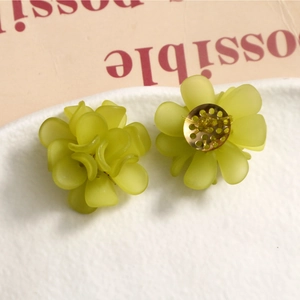 Detail of matte green floral acrylic earrings with gold center on a white textured plate