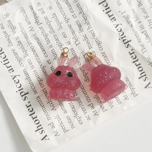 Close-up of pink translucent glittery resin bunny charms with gold loops on newspaper