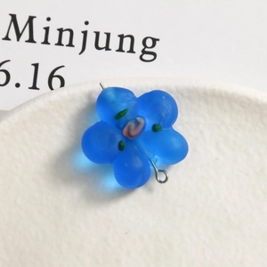 Detail of frosted blue glass flower pendant with silver loop on ceramic tray