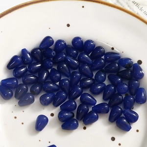 Macro shot of dark blue teardrop stones with ink-wash texture in a white ceramic dish