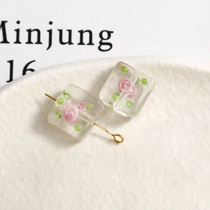 Macro detail of square frosted glass bead with pink rose motif and gold metal pin