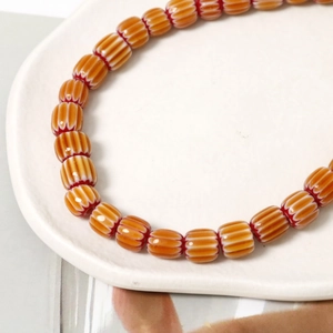 Dettaglio macro di perle in ceramica a zucca con motivi ondulati su vassoio bianco