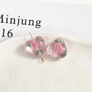 Close-up of matte pink frosted glass heart beads with painted rose patterns for DIY jewelry