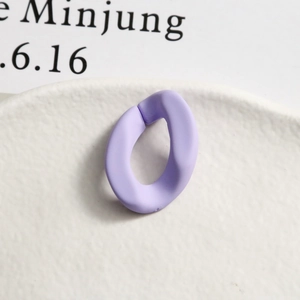 Gros plan d'une boucle ovale en résine violette mate matériau bricolage sur plateau blanc