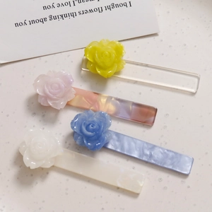 Primer plano detallado de cuatro pinzas para el cabello de acrílico en amarillo, rosa, azul y blanco