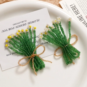 Detail of handmade beaded flower earrings with green stems and golden bow accents