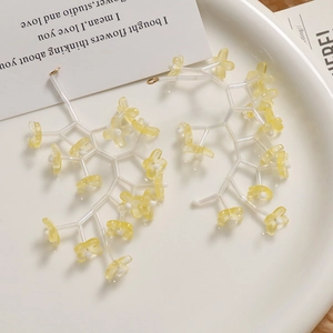 Macro detail of translucent branch-shaped earrings with yellow resin flowers on white ceramic