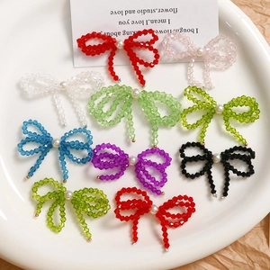 Handmade colorful crystal bow earrings with pearl center in a minimalist white plate