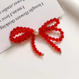 Close-up of a handmade red crystal beaded bow earring with a central white pearl detail