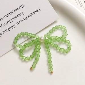 Detailed macro of green crystal bow earrings with hanging beads and central white pearl