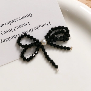 Close-up of black beaded bow earring with white pearl accent and hanging bead chains