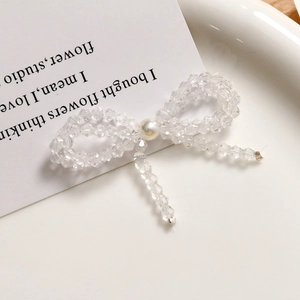 Detail of a handmade crystal bow earring featuring clear beads and a central white pearl