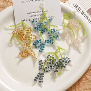 Handmade woven crystal flower earrings in four colors displayed on a white ceramic tray