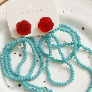 Detail of red rose earrings with light blue beaded tassels on a jewelry display card