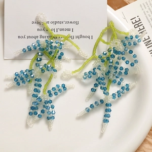 Detailed close-up of handmade beaded floral earrings with blue crystals and green seed beads
