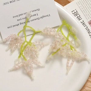 Close-up of handmade beaded floral earrings in pale pink and green on a display tray
