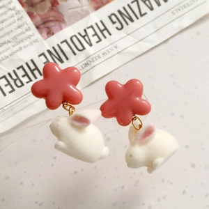 Close-up of cute pink flower earrings with white flocked rabbit pendants on newspaper
