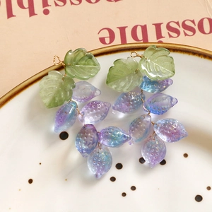 Detalle de pendientes de cristal con forma de uva y degradado púrpura con hilo de oro
