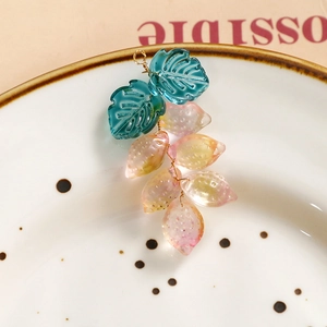 Detalle de dijes artesanales de vidrio con hojas y frutas en un plato blanco
