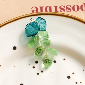 Foto macro de pendientes de hoja de cristal con frutos verde esmeralda y detalles en pan de oro