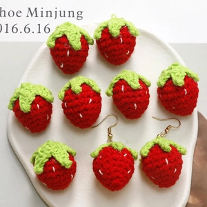 Macro shot of handmade crochet strawberry charms and earrings on a white ceramic tray