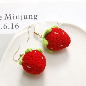 Handmade crochet strawberry drop earrings with gold hooks on a decorative plate