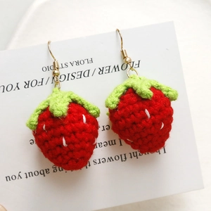 Detailed view of handmade knitted red strawberry earrings with gold metal hooks and leaf detail