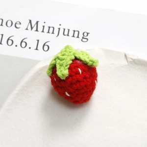 Detailed close-up of a handmade 3D knitted strawberry with green leaves and white seeds