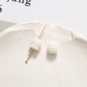 Nahaufnahme weißer Maiglöckchen-Keramikperlen für DIY-Schmuck auf einem weißen Tablett