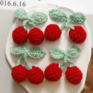 Handmade crochet red cherry charms with green leaves on white tray for DIY crafts