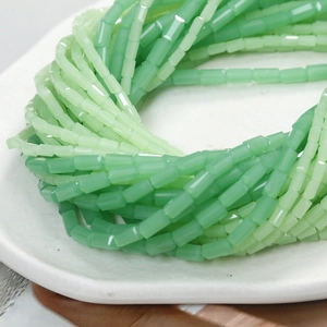Green cylindrical frosted glass beads for handmade DIY jewelry on a white ceramic tray